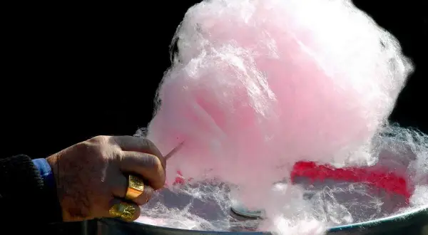 Main d'un homme fabriquant du sucre à barbe à papa rose et blanc.