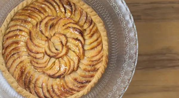 Tarte aux pommes recette : une tarte aux pommes dorée, disposée en spirale sur un plat en verre, prête à être dégustée.