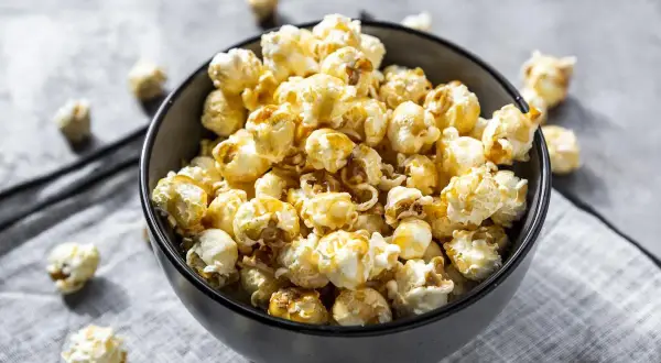 Un bol rempli de pop corn sucré, avec quelques grains éparpillés autour. Parfait pour une soirée cinéma gourmande.