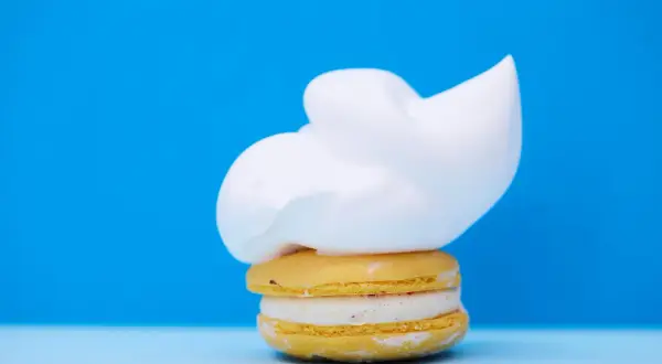 Un macaron jaune garni d'une crème blanche et surmonté d'une généreuse chantilly. Un délice qui rappelle la ganache chocolat macaron.