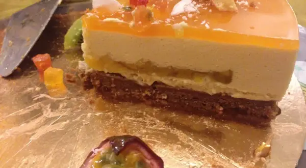 Tranche de gâteau mousseux à l'orange et au fruit de la passion, garnie de fruits et de kiwi.