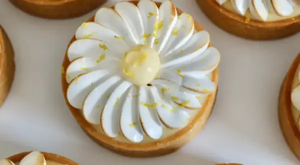 Plusieurs tartelettes au citron meringuées, décorées de zestes jaunes et d'une touche de meringue dorée. Un délice visuel pour un pochage tarte citron parfait.