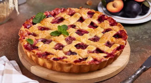 Tarte aux prunes maison, avec une croûte dorée et une garniture généreuse de fruits rouges, décorée de feuilles de menthe.
