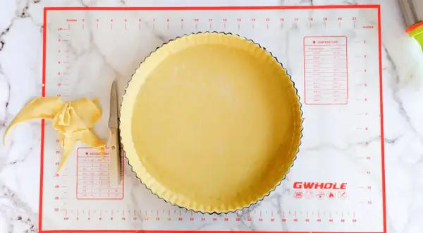 Préparation d'une conservation pâte brisée maison dans un moule à tarte, avec des chutes de pâte et un couteau.