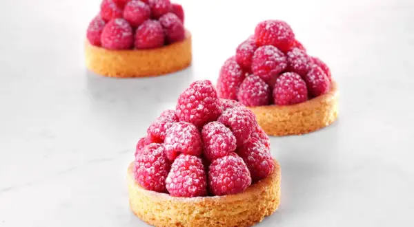 Trois tartelettes sablé breton garnies de framboises fraîches saupoudrées de sucre glace. Une invitation à la gourmandise.