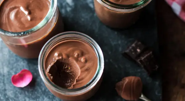 Trois pots de crème chocolat maison, on voit une cuillère avec une touche de mousse et des carrés de chocolat noir.