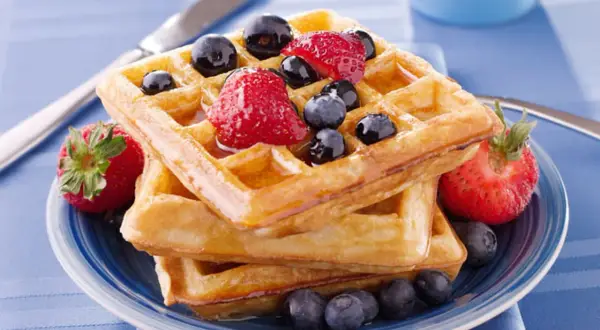 Pile de gaufres dorées garnies de fraises et myrtilles, un délice pour la meilleure recette de gaufres.