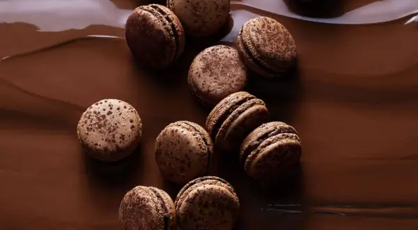 Douceurs chocolatées pour une recette macaron chocolat parfaite. Ces macarons aux éclats de cacao reposent sur un lit de chocolat fondant.