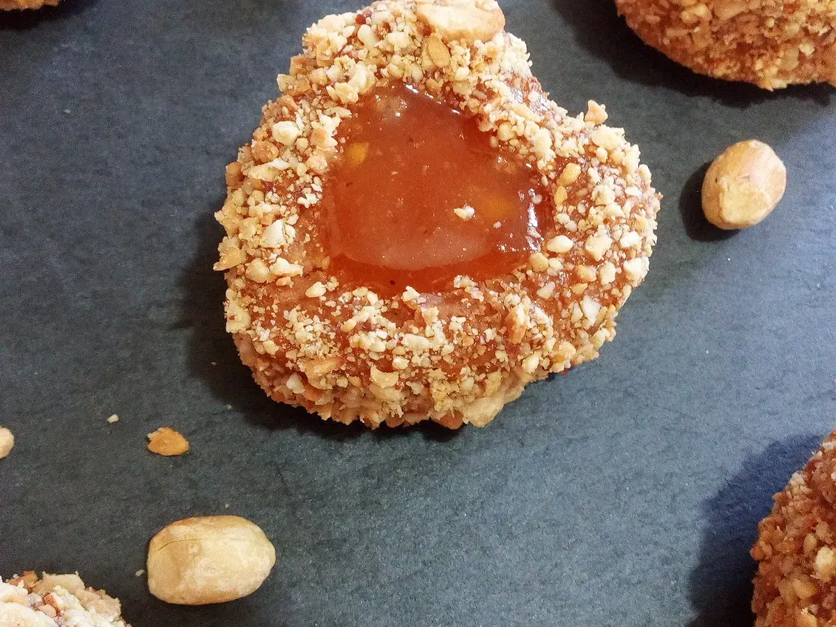 Un sablé algérien à la confiture, enrobé de noisettes concassées, sur fond sombre.