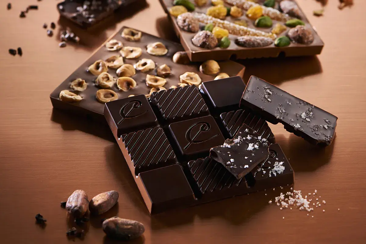 Tablettes de chocolat noir artisanal, aux noisettes, aux fruits confits et au sel. Une invitation à découvrir comment faire du chocolat noir.