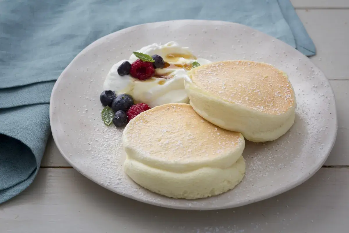 Deux pancakes aériens et moelleux saupoudrés de sucre glace, servis avec de la crème fouettée, des baies et du sirop.