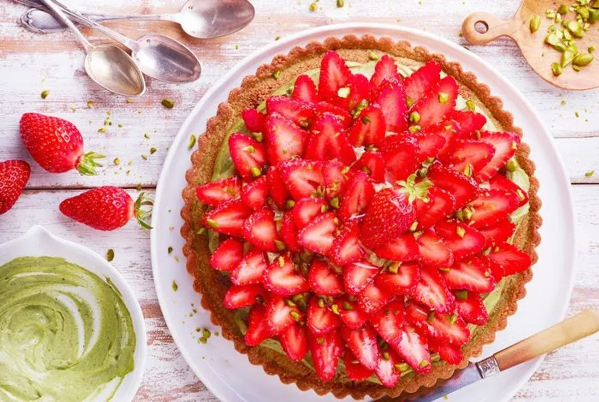 Tarte fraise pistache, une gourmandise aux couleurs vives, garnie de fraises fraîches et de pistaches concassées sur une crème onctueuse.