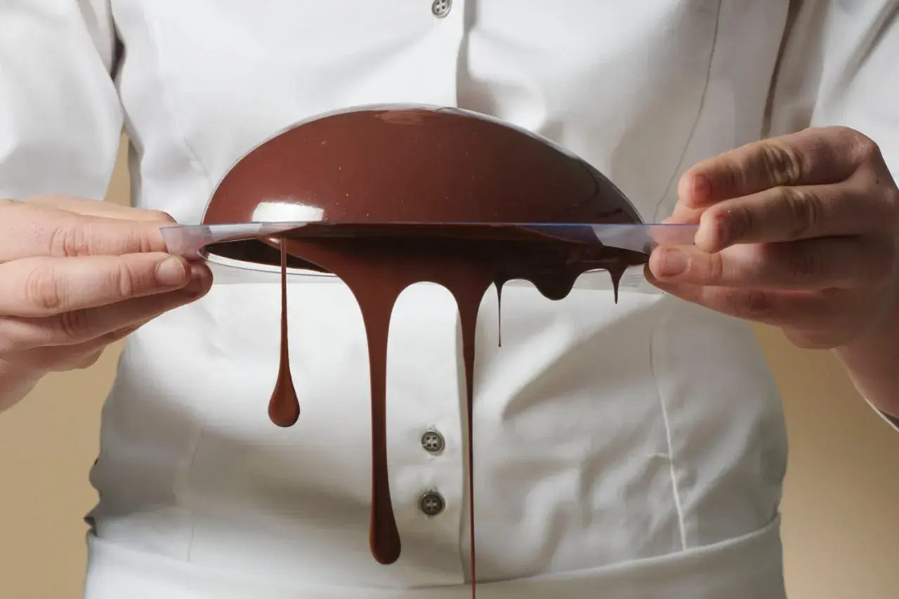 Comment faire du chocolat au lait : une demi-sphère de chocolat coule d'un moule transparent tenu par des mains.