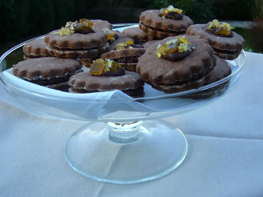 Gourmandes bouchées de biscuits fourrés chocolat, ornées de zestes d'agrumes confits, présentées dans une coupe en verre.
