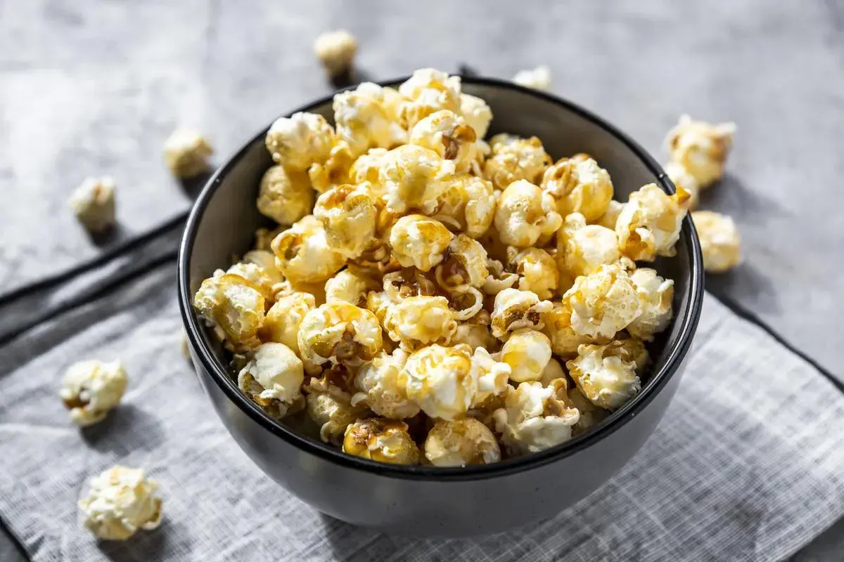 Un bol rempli de pop corn sucré, avec quelques grains éparpillés autour. Parfait pour une soirée cinéma gourmande.