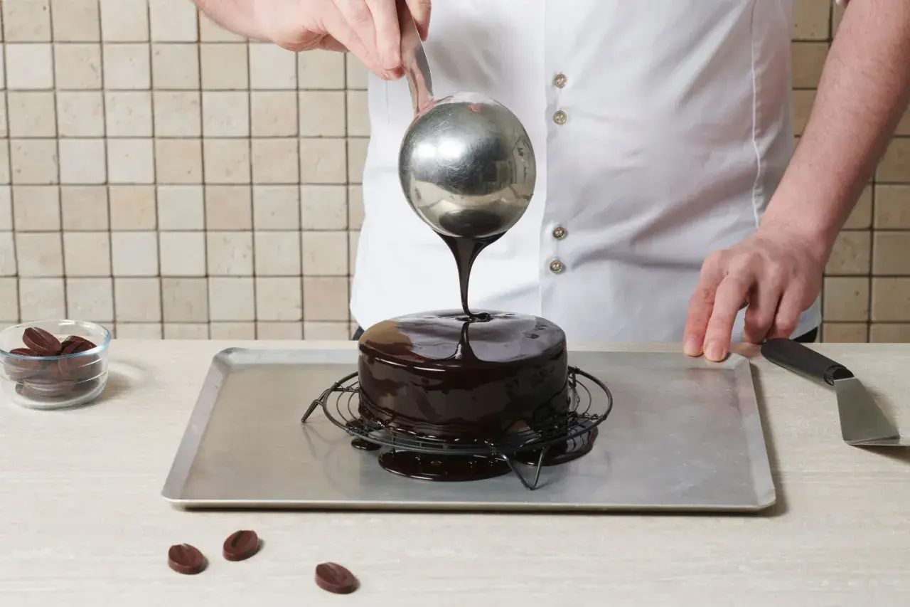 Un chef verse un glaçage miroir brillant sur un gâteau au chocolat.