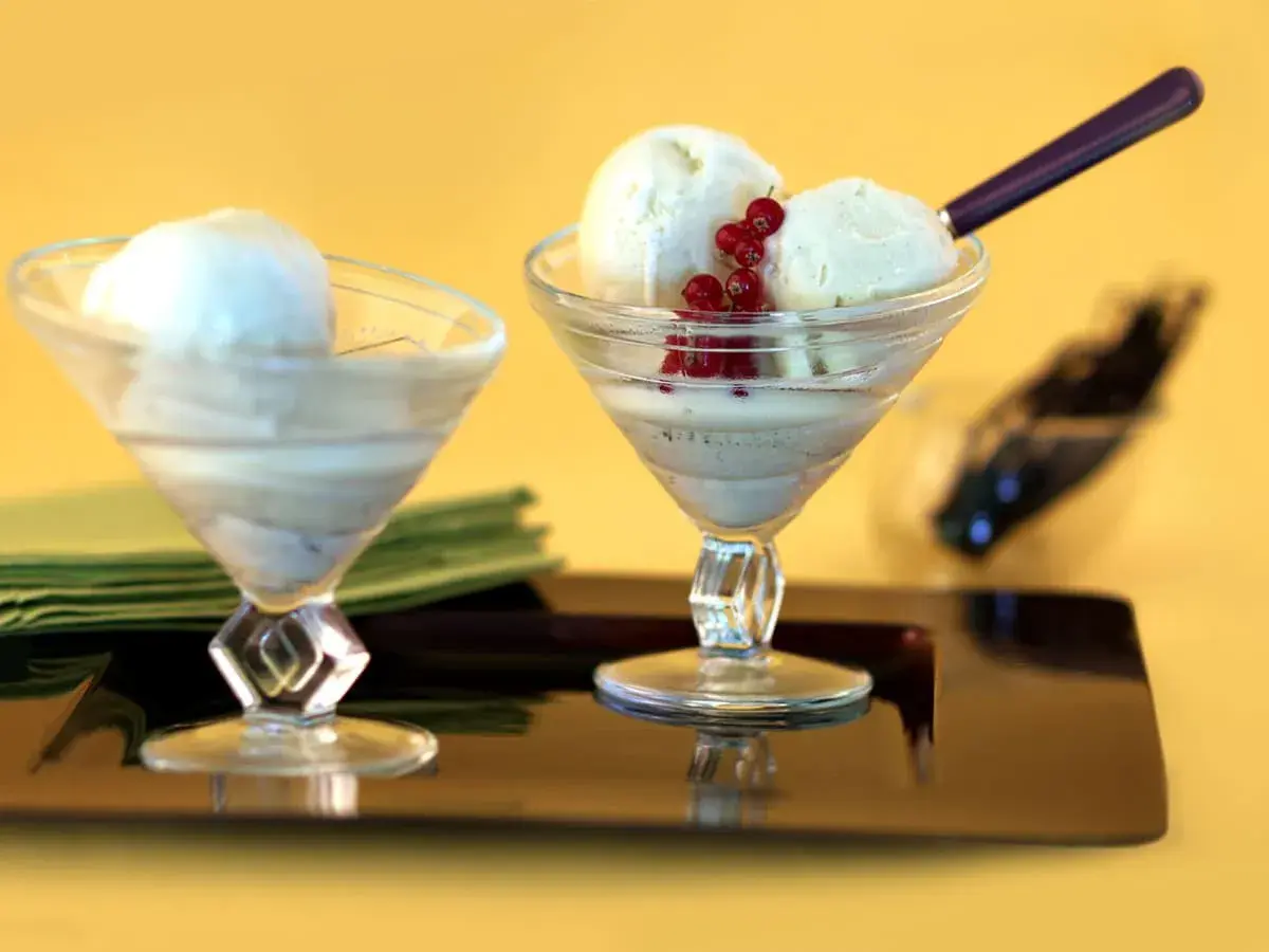 Deux coupes de **dessert glacé vanille** ornées de groseilles, sur un plateau sombre.