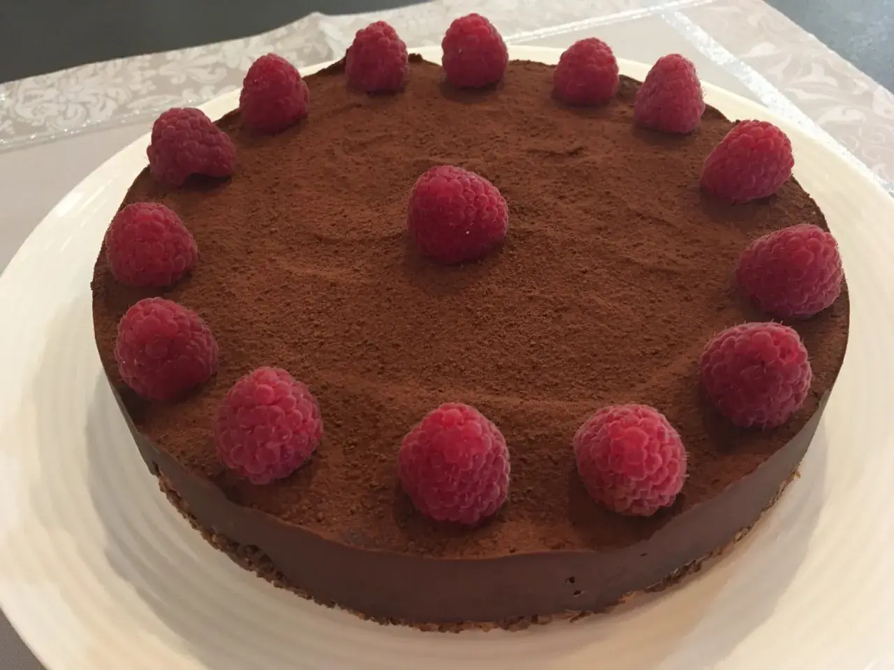 Tarte chocolat framboise, une gourmandise visuellement irrésistible, saupoudrée de cacao et ornée de framboises fraîches.