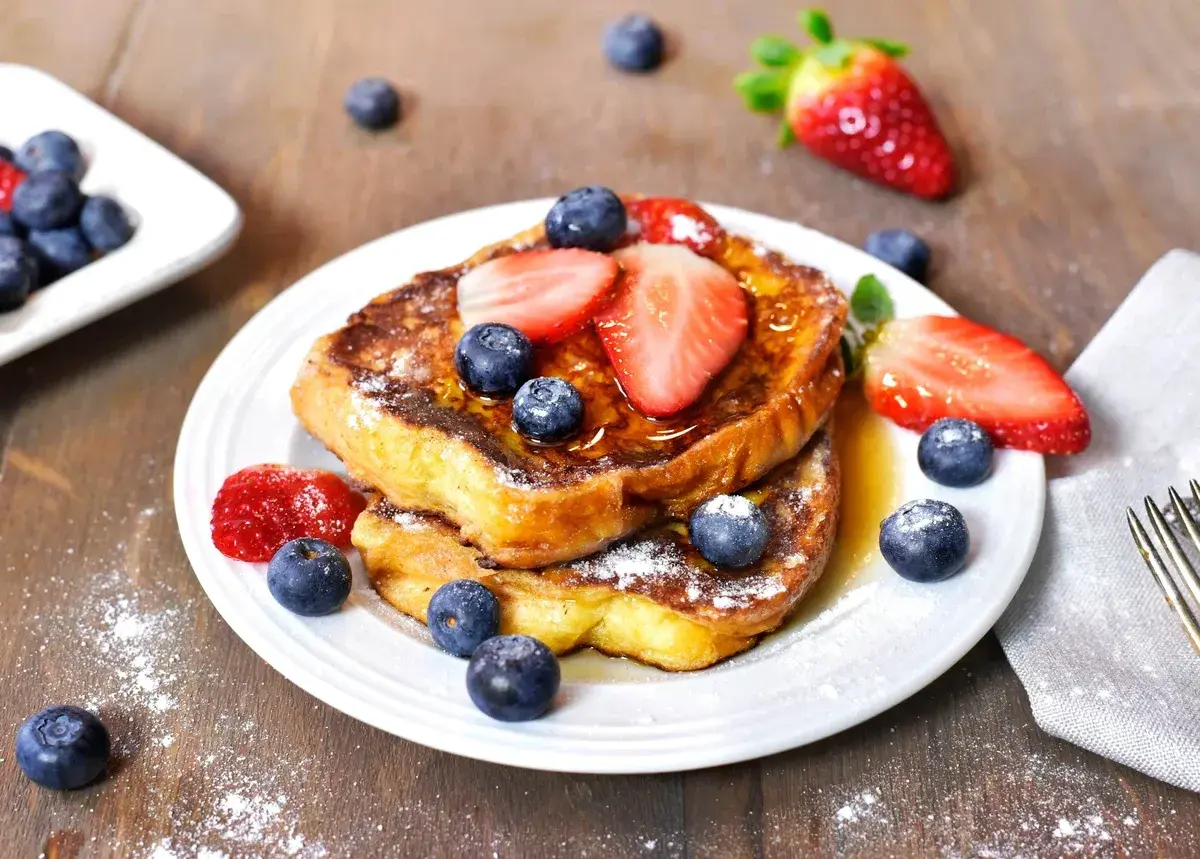 Un délicieux pain perdu garni de fraises et de myrtilles, saupoudré de sucre glace. Un petit-déjeuner gourmand.