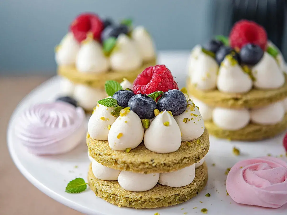 Délicieux petits gâteaux pistache-chocolat blanc, garnis de fruits rouges et de menthe. Parfait pour une recette ganache montée chocolat blanc.