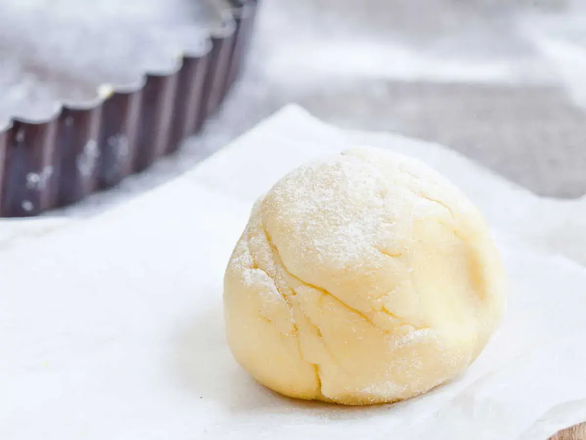 Une boule de pâte sucrée amande, saupoudrée de sucre glace, prête à être utilisée dans un moule à tarte.