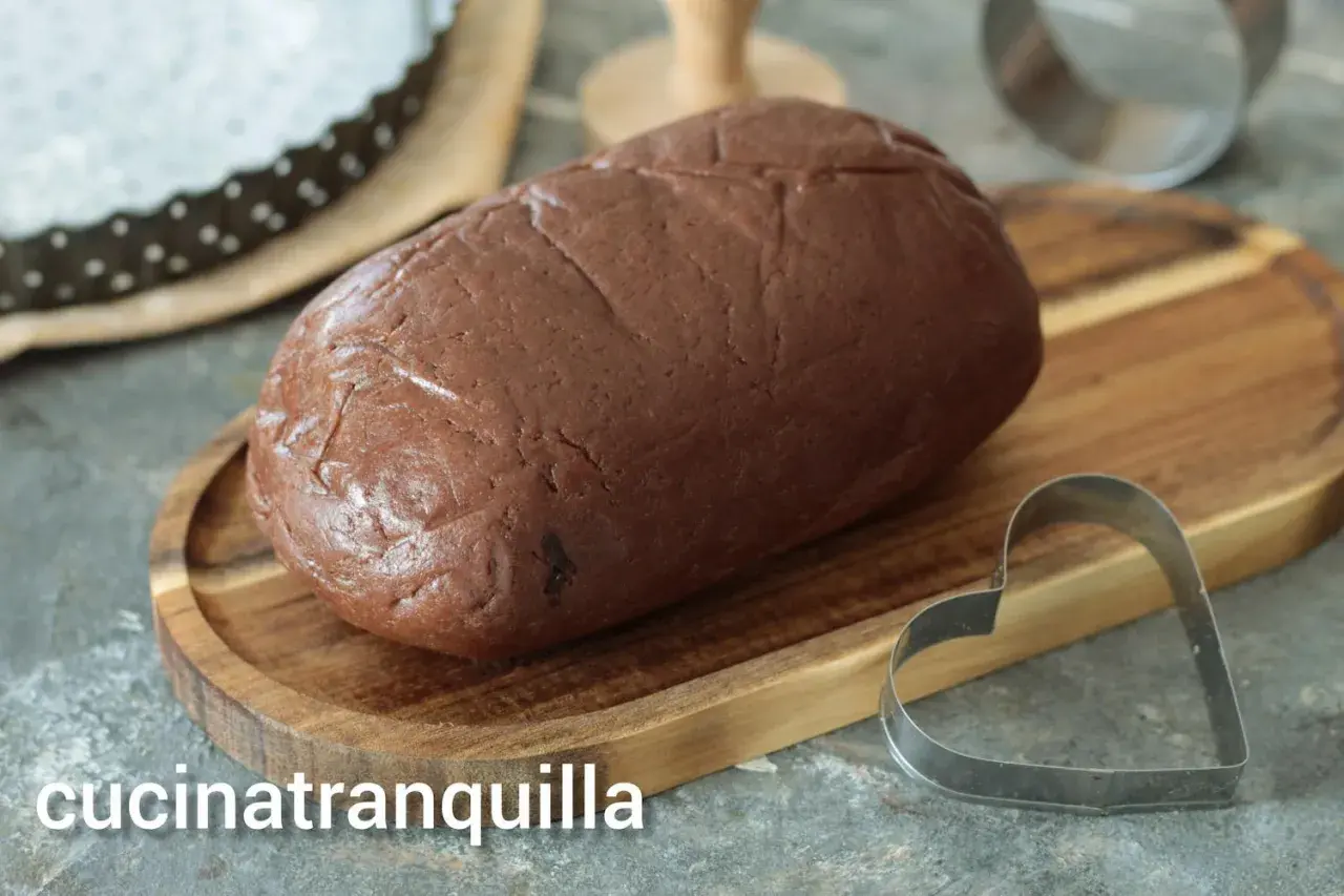 Pâte sablée au chocolat prête à être façonnée. Un emporte-pièce en forme de cœur est à proximité, suggérant de délicieuses créations.