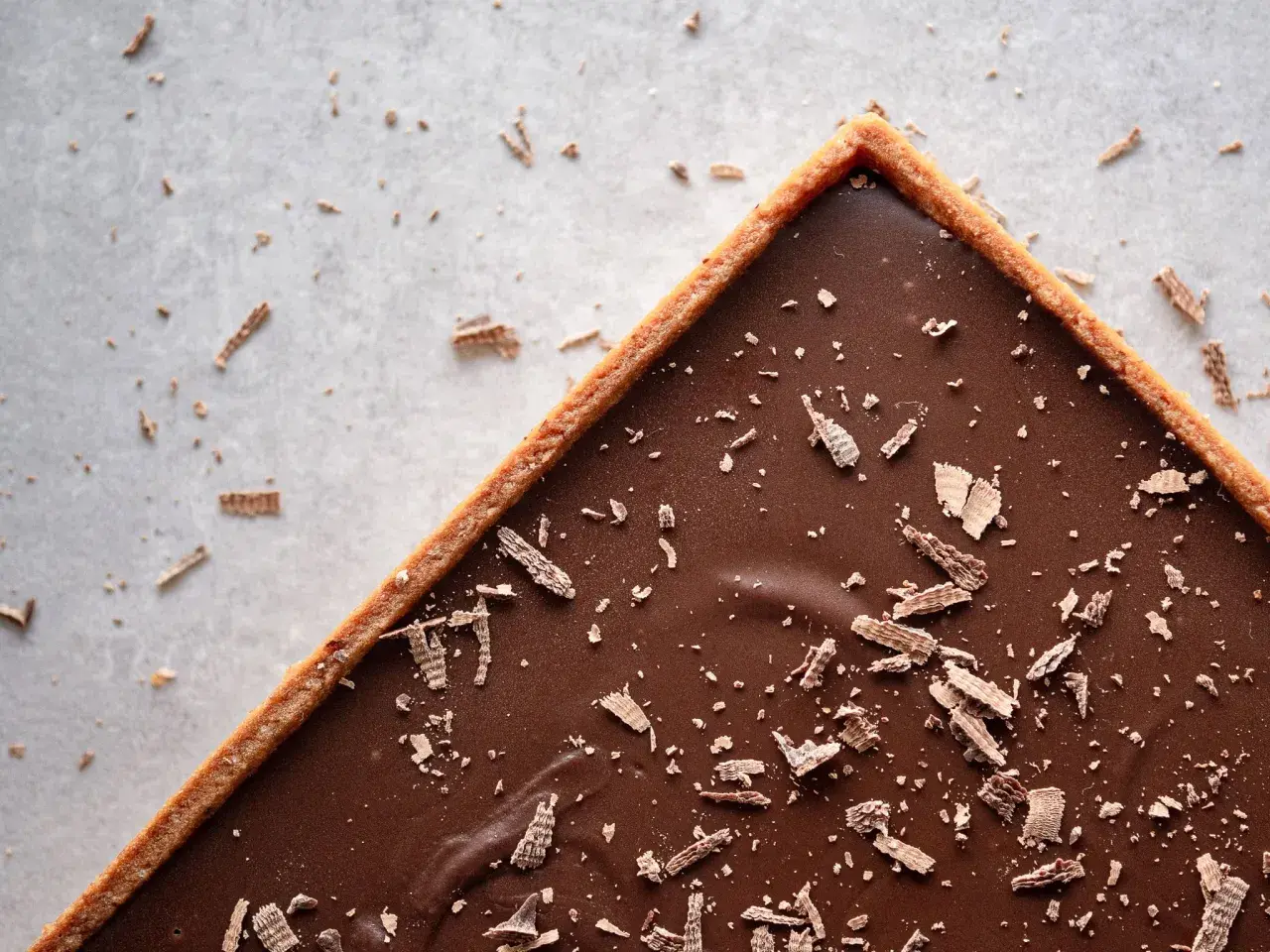 Une délicieuse tarte au chocolat vegan, garnie de copeaux de chocolat, sur un fond clair parsemé de miettes.
