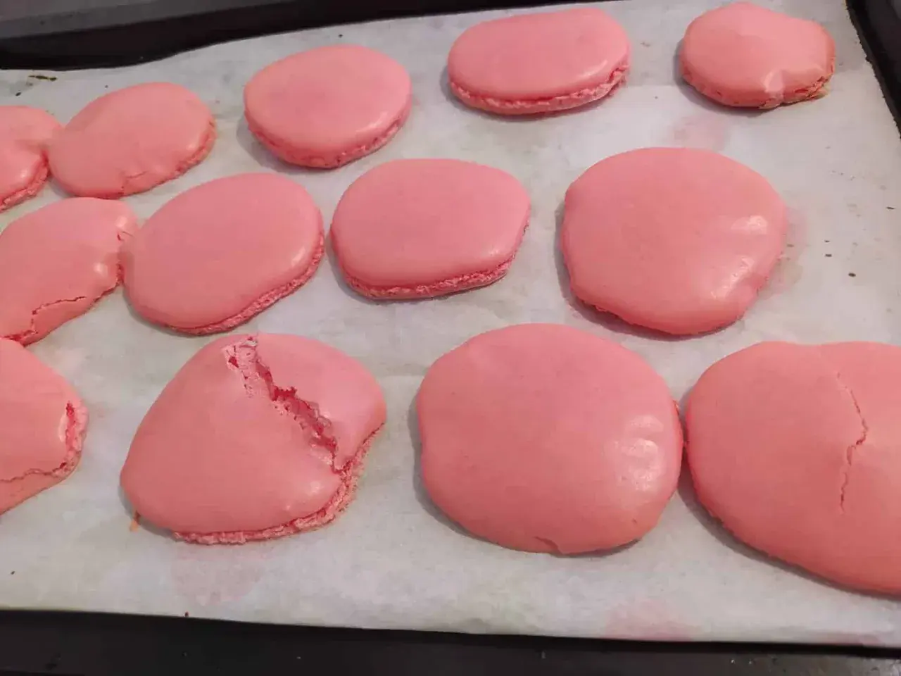 Coques de macarons roses sur une plaque de cuisson. Certaines sont parfaites, d'autres craquent, illustrant pourquoi les macarons craquent.