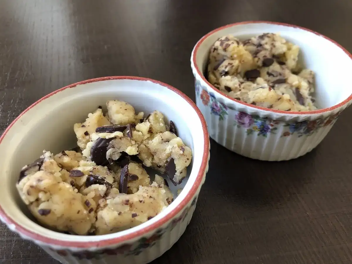 Deux ramequins remplis de pâte à cookie aux pépites de chocolat, prêts à être dégustés.