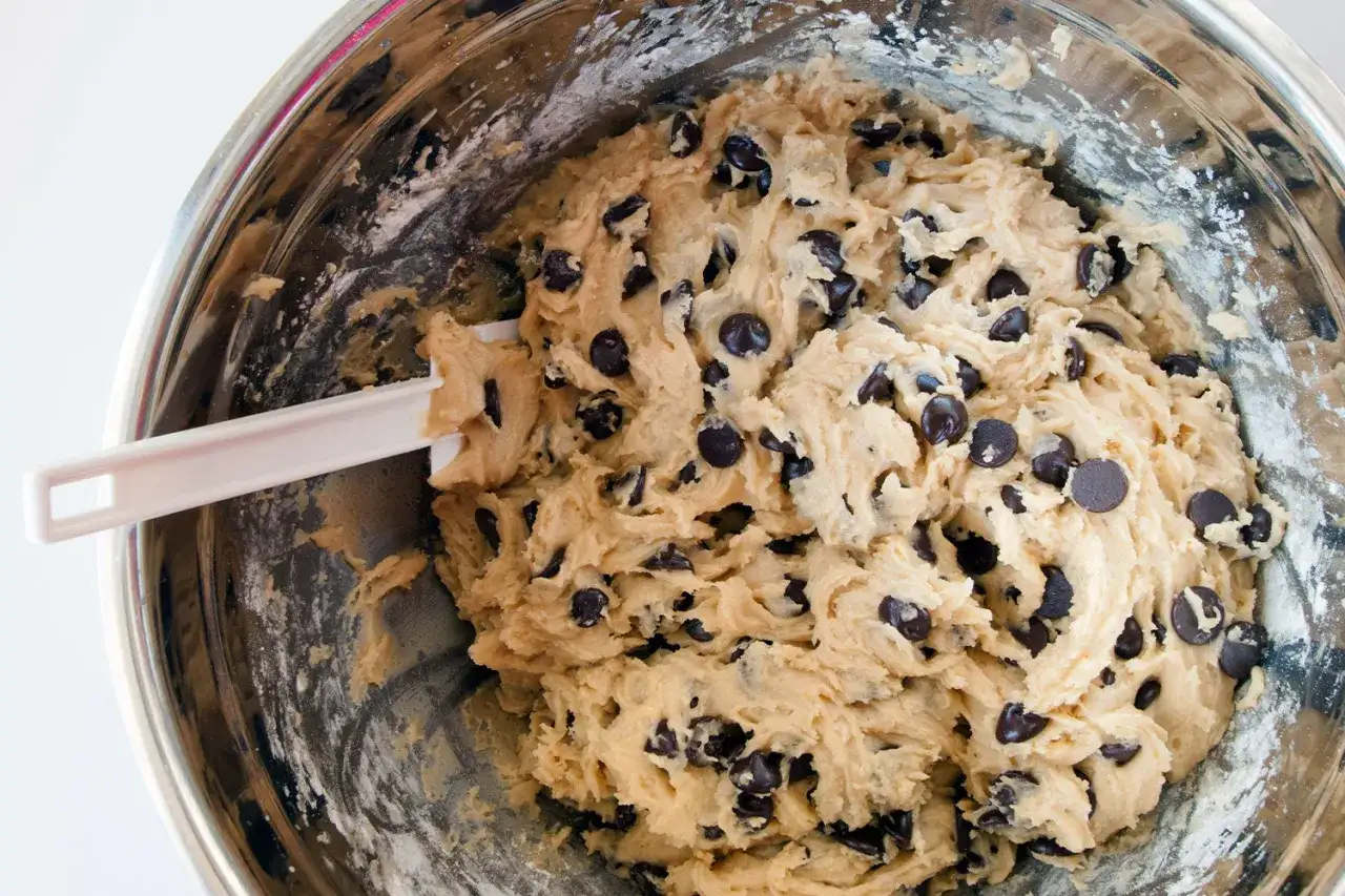 Pâte à cookie maison, généreusement garnie de pépites de chocolat, prête à être transformée en délices gourmands. Une spatule blanche repose dans le bol.