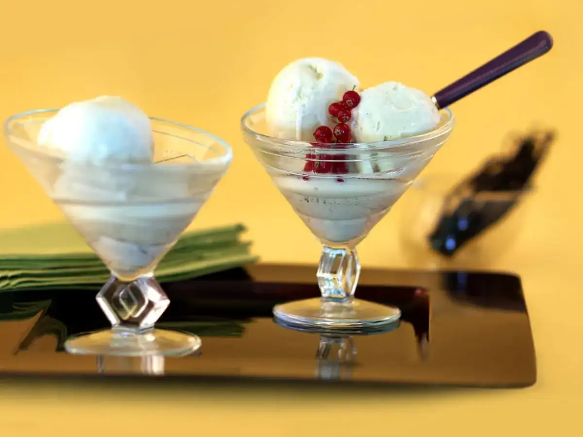 Deux coupes de **dessert glacé vanille** ornées de groseilles, sur un plateau sombre.