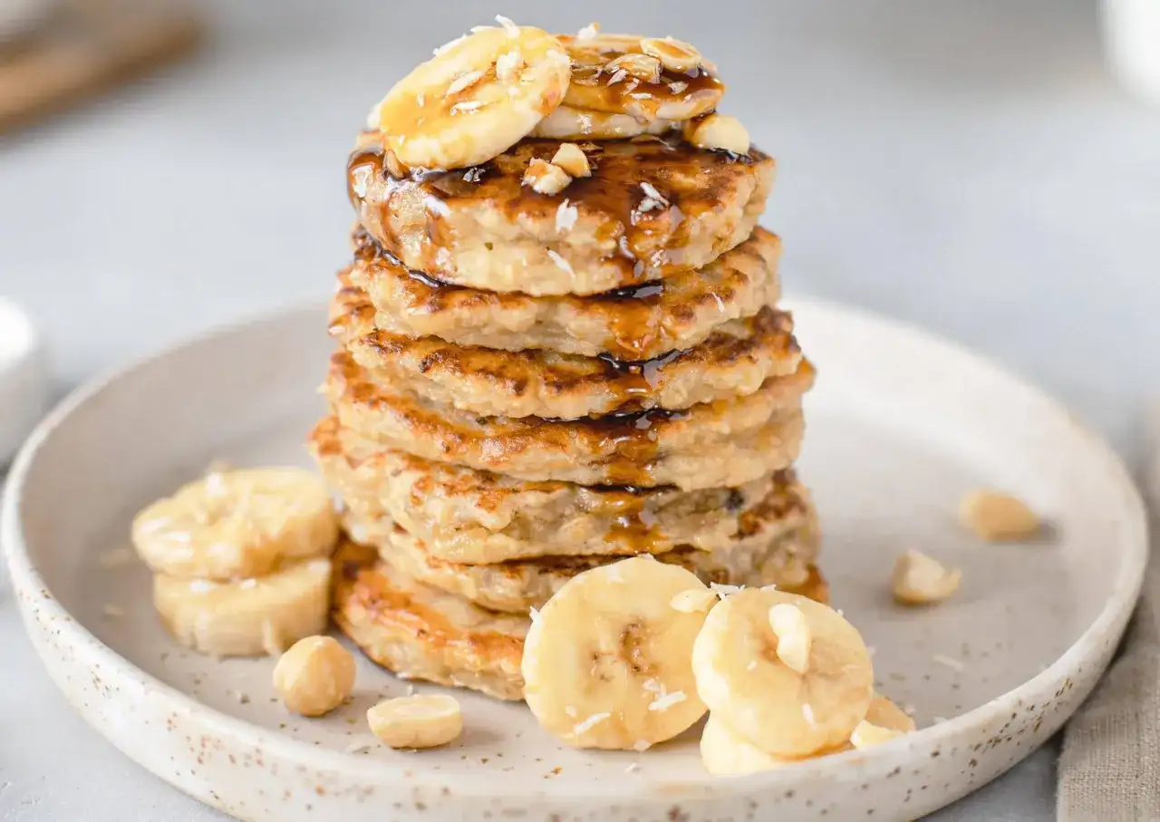 Pile de pancakes flocon d'avoine, garnis de rondelles de banane, de noix et nappés de sirop. Un délice sain pour le petit-déjeuner.