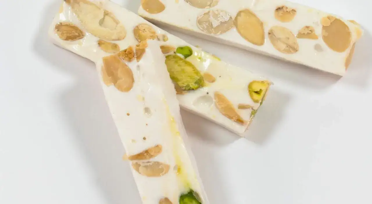Trois barres de nougat Montélimar recette, garnies d'amandes et de pistaches, sur fond blanc.
