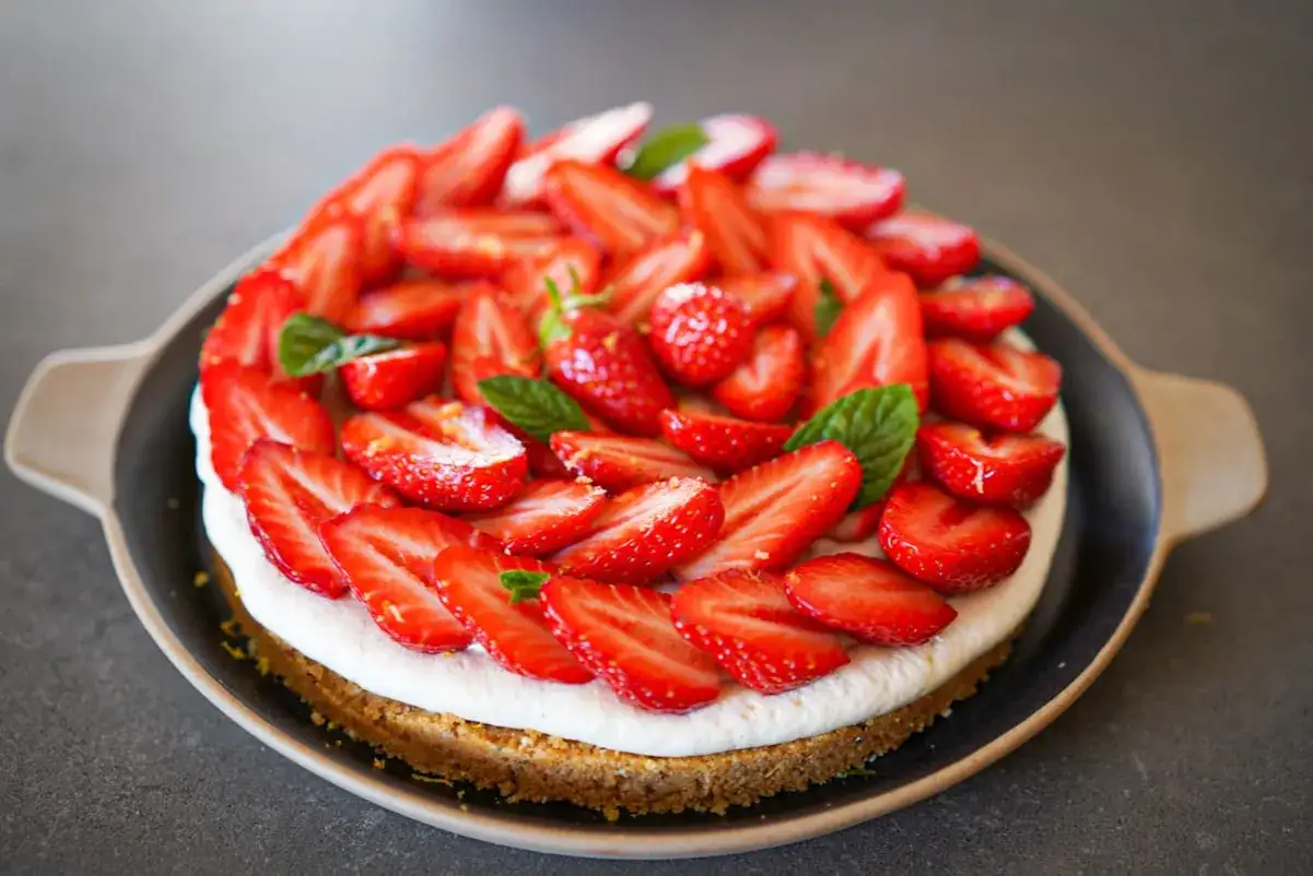 Tarte aux fraises sans cuisson, garnie de fraises fraîches et de feuilles de menthe, sur un fond sombre.