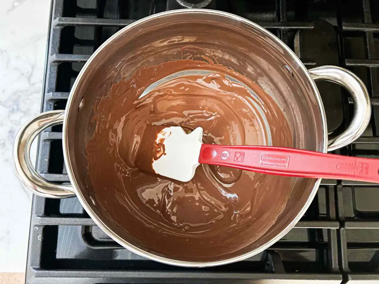 Comment faire fondre du chocolat : une spatule mélange du chocolat fondu dans une casserole sur une cuisinière.