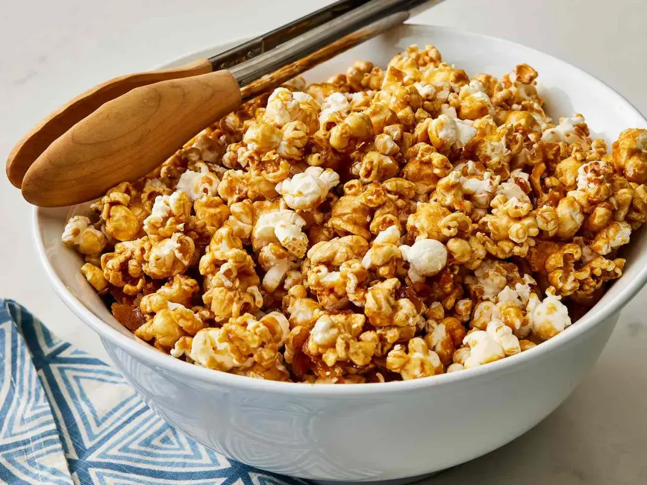 Un bol rempli de pop corn sucré, prêt à être dégusté avec des pinces en bois.