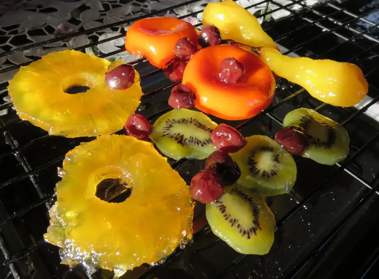 Des fruits confits brillants : rondelles d'ananas, kiwis, cerises et formes orangées. Une recette pour comment faire des fruits confits.