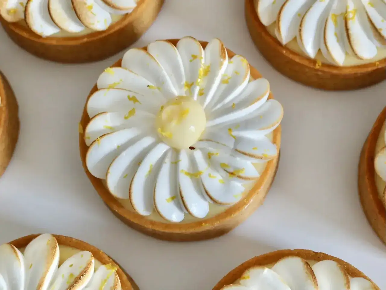 Plusieurs petites tartelettes au citron meringuées, ornées de zestes jaunes, attendent d'être dégustées.