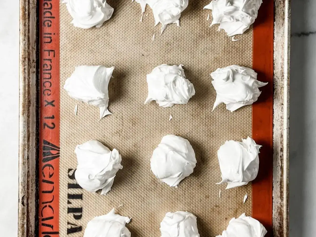 Petites meringues italiennes pr&ecirc;tes &agrave; cuire sur une plaque recouverte de papier sulfuris&eacute;.