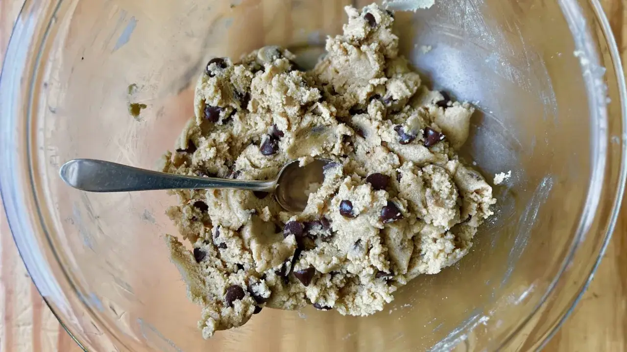 Pâte à cookie aux pépites de chocolat dans un bol en verre, avec une cuillère.