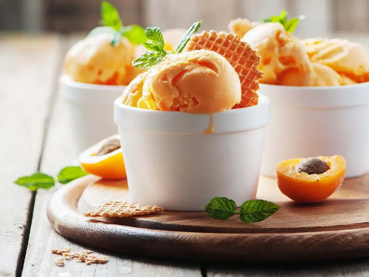 Douceur fruitée : trois coupes de glace à la pêche, garnies de menthe fraîche et de gaufrettes croustillantes, avec des abricots mûrs en accompagnement.