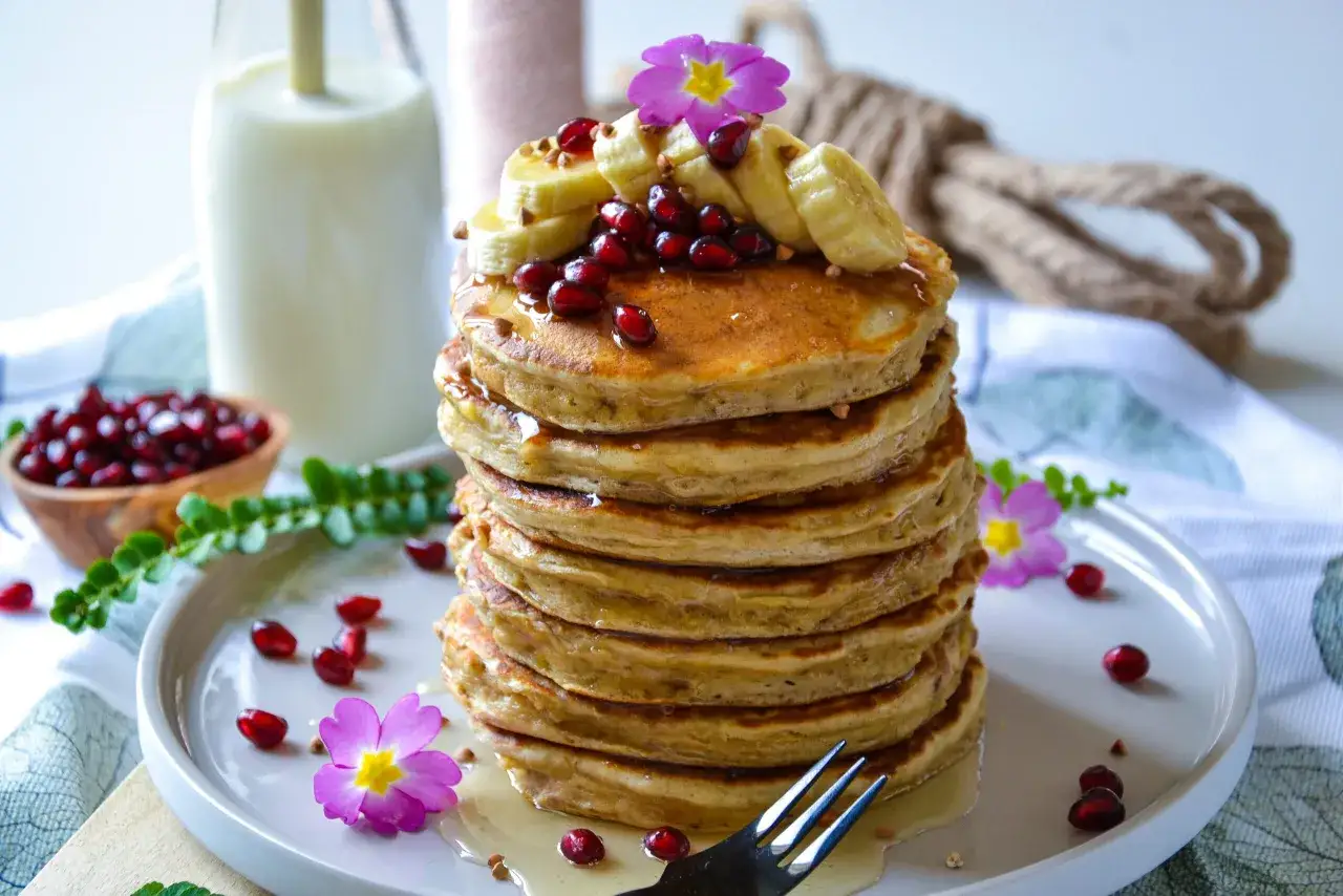 Pile de pancake banane, garnie de fruits rouges et de fleurs roses. Un délice pour le petit-déjeuner.