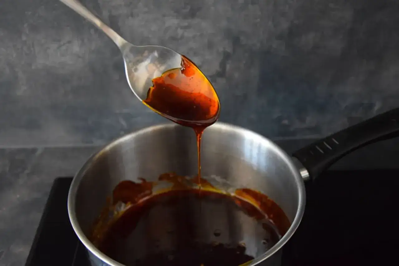 Une cuill&egrave;re verse un caramel liquide dor&eacute; dans une casserole. La texture sirupeuse promet une douceur gourmande.