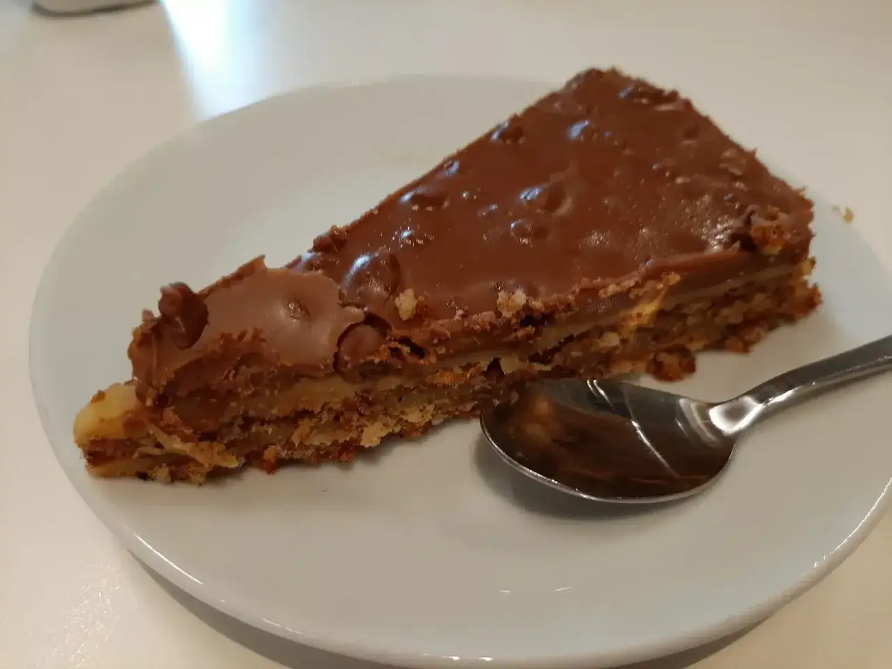 Une part de tarte aux daims, avec sa croûte croustillante et son glaçage au chocolat brillant, attend patiemment une cuillère sur une assiette blanche.