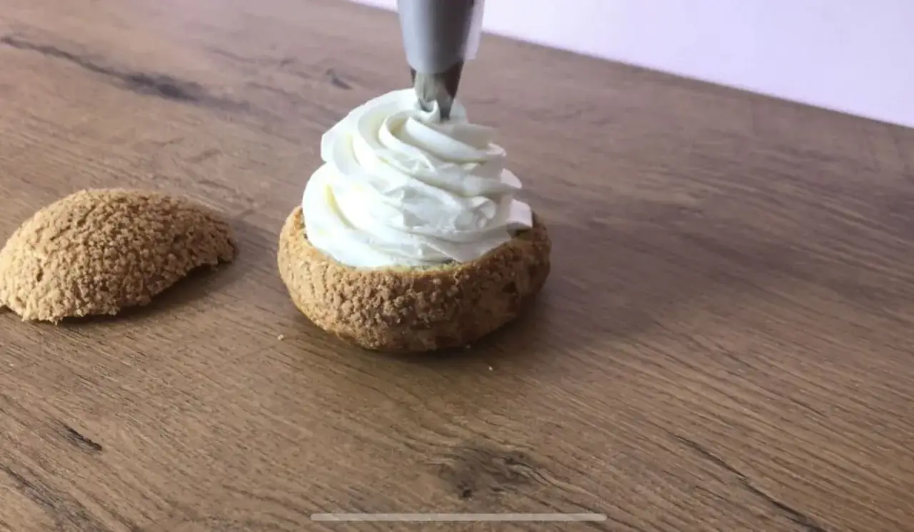 Une poche &agrave; douille d&eacute;pose une g&eacute;n&eacute;reuse cr&egrave;me chantilly sur un chou craquelin. Un autre chou est pos&eacute; &agrave; c&ocirc;t&eacute;.