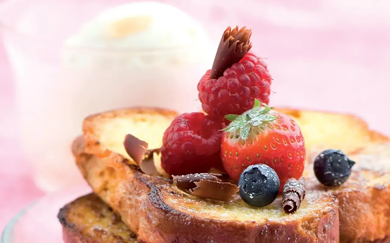 Pain perdu doré, garni de framboises, fraises, myrtilles et copeaux de chocolat. Un délice sucré.