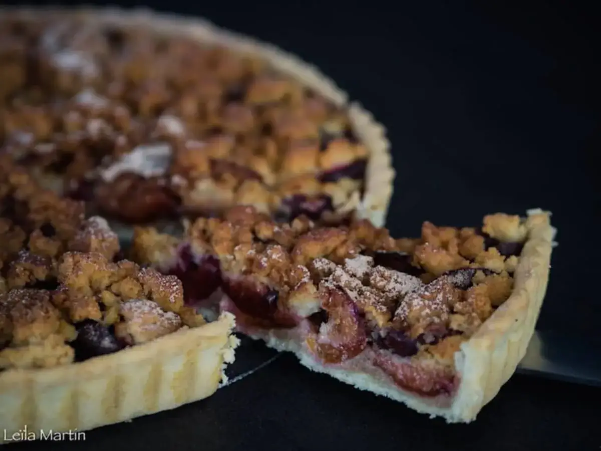 Une part de tarte aux quetsches allemande, avec sa pâte dorée et sa garniture aux fruits rouges, saupoudrée de sucre glace.