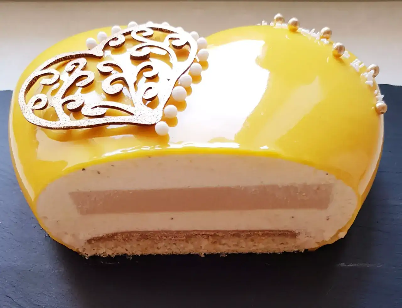 Entremet c&oelig;ur jaune vif, d&eacute;cor&eacute; d'une arabesque dor&eacute;e et de perles. L'int&eacute;rieur r&eacute;v&egrave;le des couches onctueuses et un insert caramel beurre sal&eacute;.