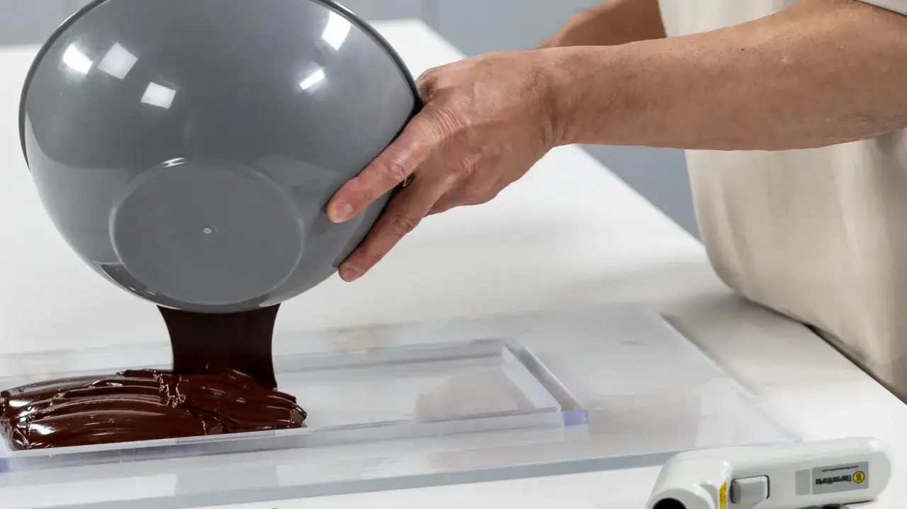 Verser du chocolat noir fondu dans un moule pour le tempérer. Un thermomètre est visible à proximité.
