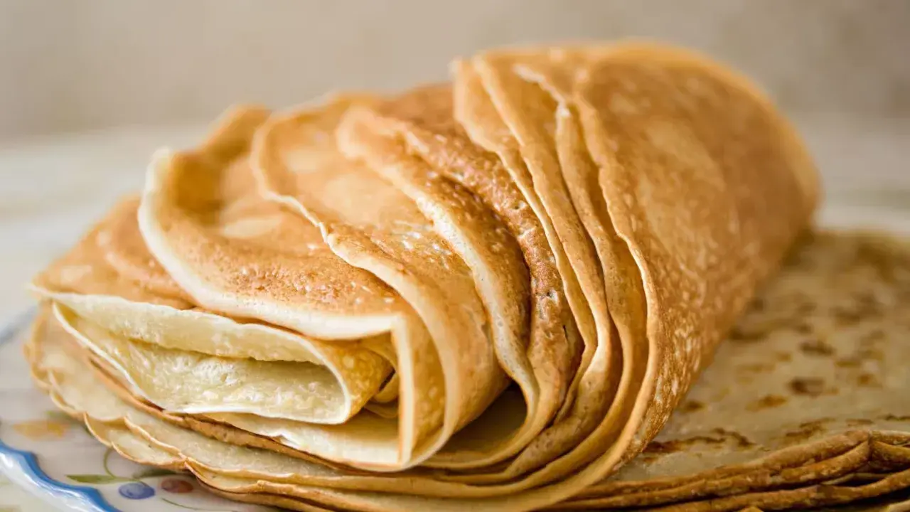 Pile de crêpes dorées, parfaites pour une recette pâte à crêpe facile. Elles sont empilées sur une assiette décorée.
